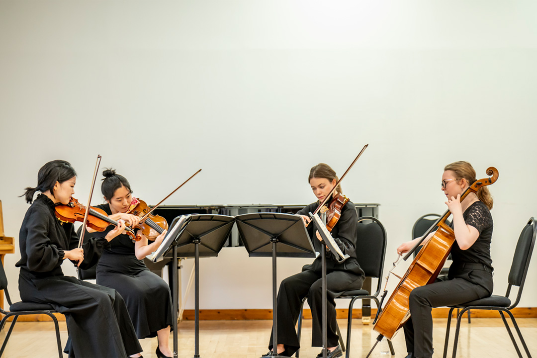 A group of string players performing in a quartet on a stage.